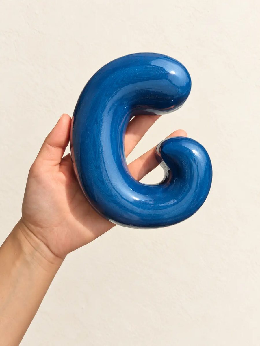 Letra G azul con acabado brillante, en la mano